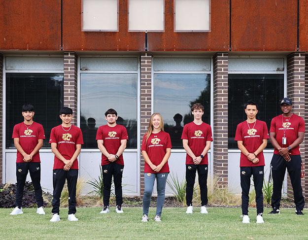 Cross country team stands outside a campus building with their coach